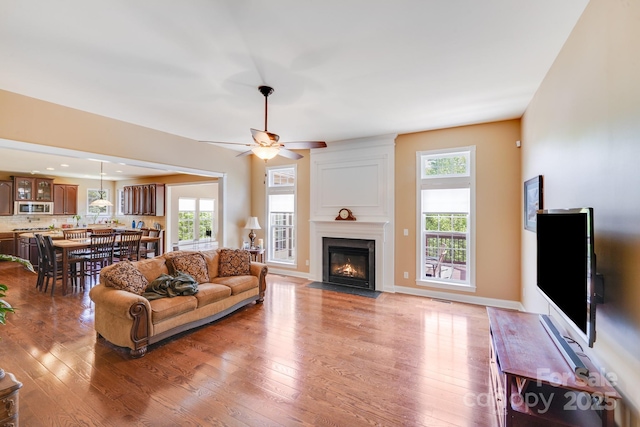 living room featuring a fireplace with flush hearth, ceiling fan, light wood finished floors, and visible vents
