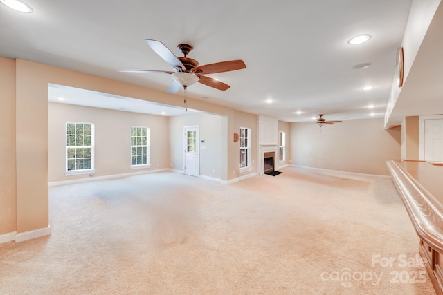 unfurnished living room with light colored carpet, a ceiling fan, recessed lighting, a fireplace with flush hearth, and baseboards