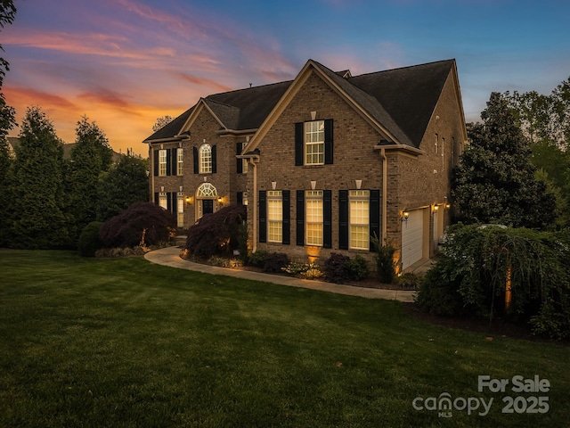 georgian-style home featuring a garage, brick siding, and a front yard