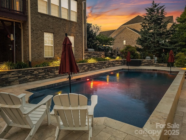 pool at dusk featuring an outdoor pool and a patio area