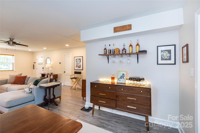 living area with baseboards, dark wood-type flooring, recessed lighting, a bar, and a ceiling fan