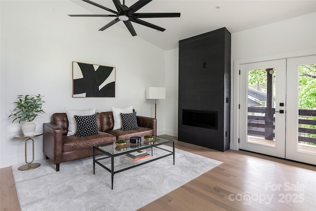 living area with french doors, a ceiling fan, a fireplace, wood finished floors, and lofted ceiling
