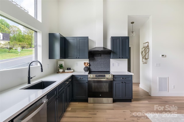 kitchen featuring appliances with stainless steel finishes, a sink, light wood finished floors, a towering ceiling, and visible vents