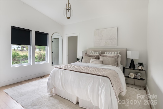 bedroom featuring baseboards, vaulted ceiling, visible vents, and light wood-style floors