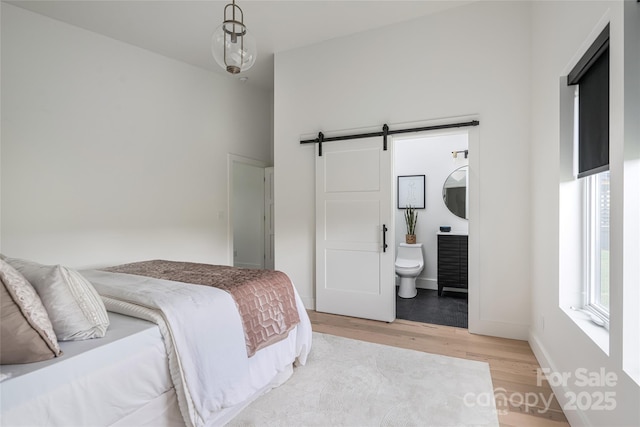 bedroom with baseboards, a barn door, light wood finished floors, and ensuite bath