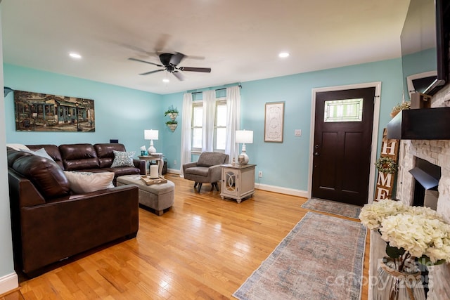 living room featuring a ceiling fan, baseboards, a stone fireplace, and light wood-style floors