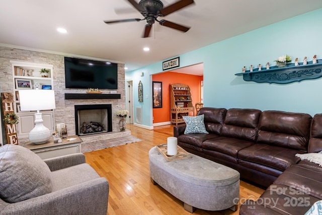 living room featuring visible vents, wood finished floors, a stone fireplace, built in shelves, and a ceiling fan