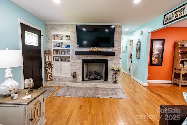 living room featuring a fireplace, built in shelves, baseboards, wood finished floors, and visible vents