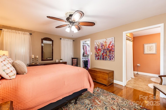 bedroom featuring a closet, wood finished floors, baseboards, ceiling fan, and a spacious closet