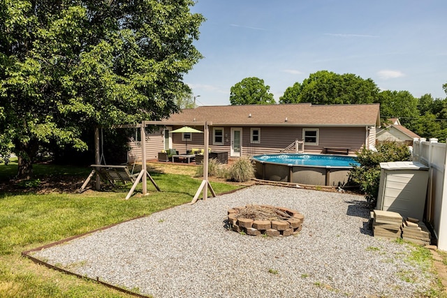 rear view of house with a fire pit, an outdoor pool, and a yard