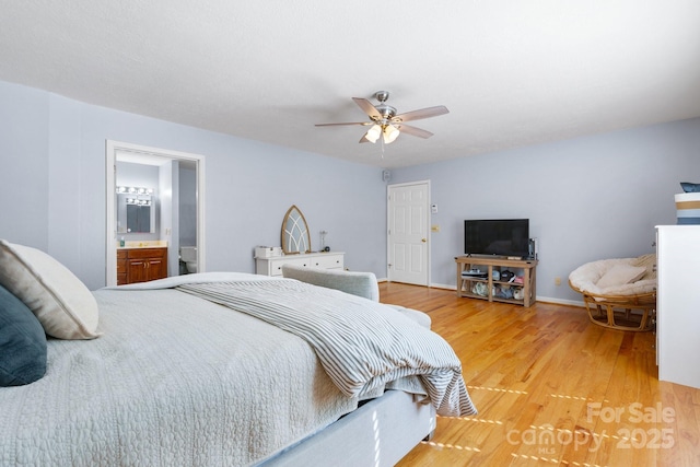 bedroom with a ceiling fan, baseboards, ensuite bath, and light wood-style floors