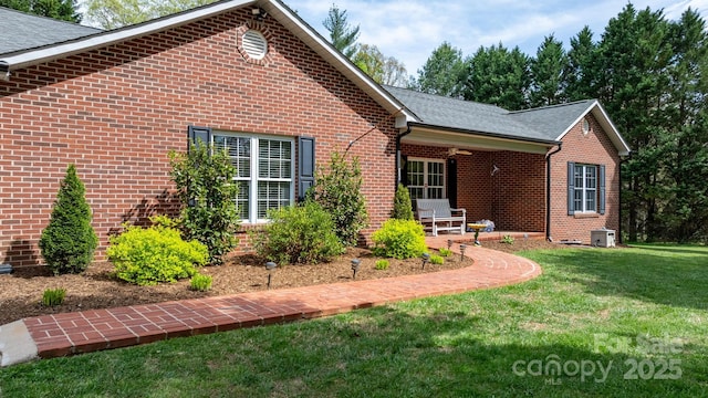 view of front facade featuring a patio, a shingled roof, a front yard, and brick siding