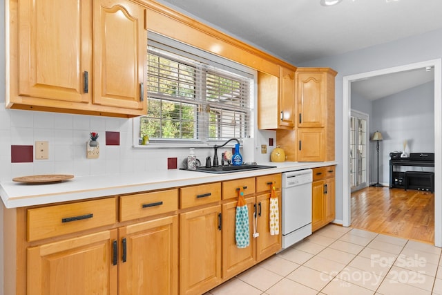 kitchen featuring backsplash, dishwasher, a sink, light countertops, and light tile patterned floors