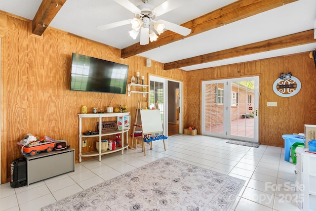 interior space with a ceiling fan, beamed ceiling, wood walls, and plenty of natural light
