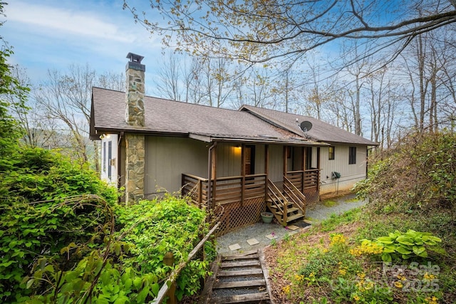 view of front of home featuring stone siding, a chimney, stairway, a porch, and roof with shingles