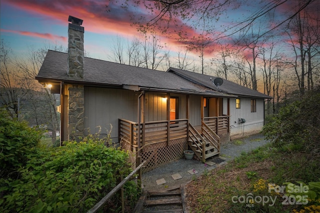 view of front of home featuring covered porch, roof with shingles, stairs, and a chimney
