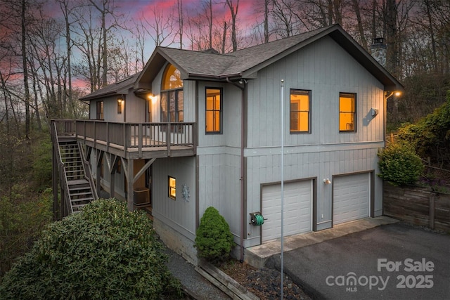 view of front of home with aphalt driveway, a garage, stairs, a wooden deck, and roof with shingles