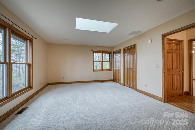 spare room featuring light colored carpet, a skylight, baseboards, and visible vents