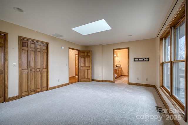 unfurnished bedroom featuring a skylight, light carpet, baseboards, and ensuite bathroom