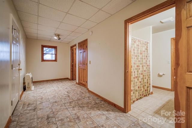 hallway featuring heating unit, a drop ceiling, and baseboards
