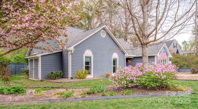 view of side of property with a lawn, fence, and a shingled roof