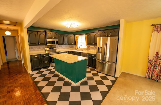 kitchen featuring backsplash, appliances with stainless steel finishes, a center island, a sink, and light countertops