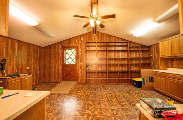 interior space featuring a ceiling fan, wood walls, built in shelves, and lofted ceiling