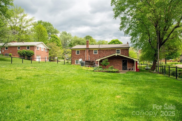 rear view of house with a fenced backyard, a chimney, a lawn, and brick siding