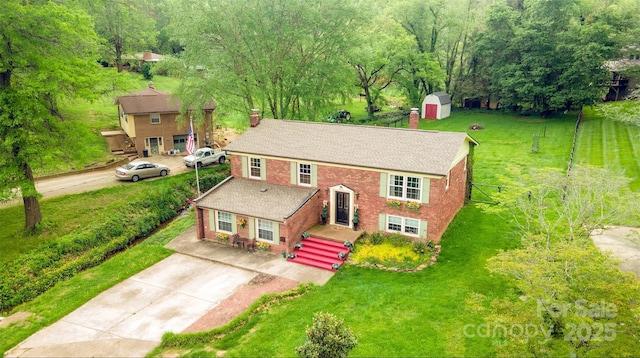 bi-level home featuring a storage unit, brick siding, a chimney, concrete driveway, and an outdoor structure