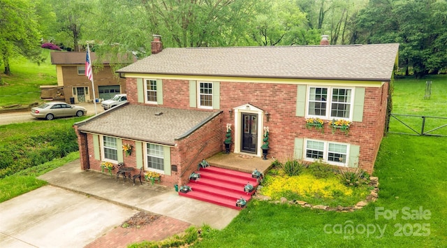 raised ranch with brick siding, a front yard, a chimney, and roof with shingles