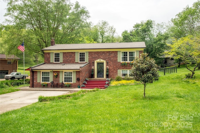 bi-level home with brick siding, a chimney, and a front lawn