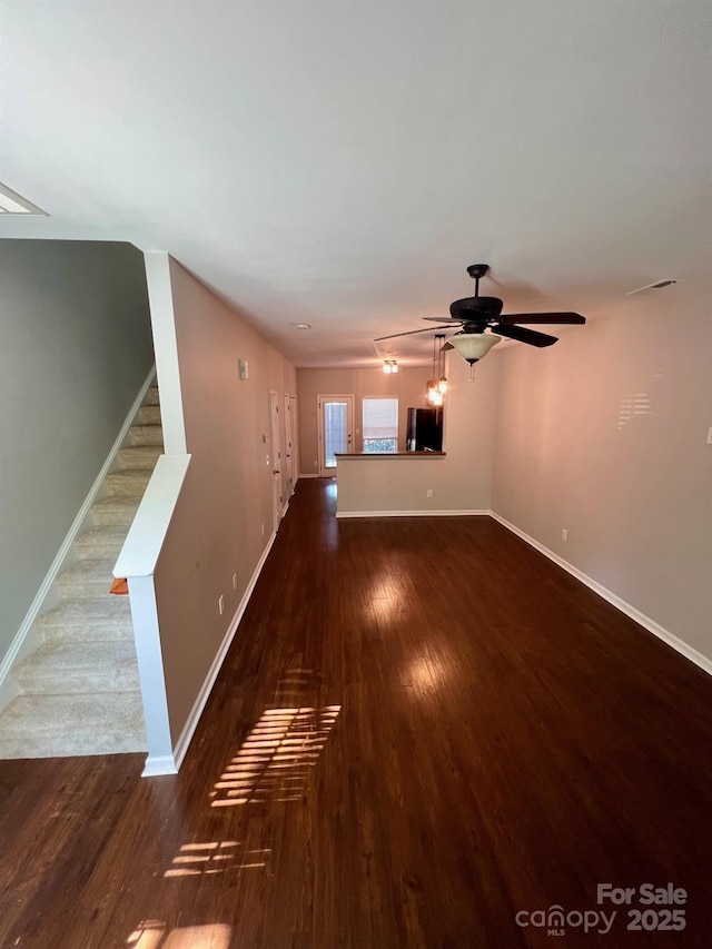 unfurnished living room featuring stairs, a ceiling fan, baseboards, and wood finished floors