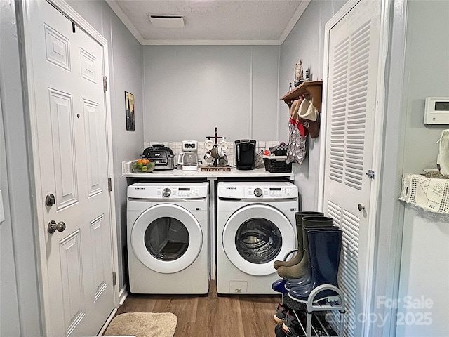 washroom with laundry area, ornamental molding, wood finished floors, visible vents, and washing machine and dryer