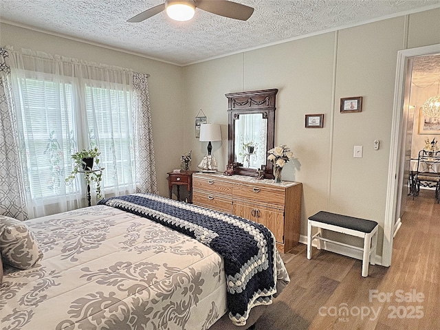 bedroom featuring ornamental molding, wood finished floors, baseboards, a textured ceiling, and a ceiling fan