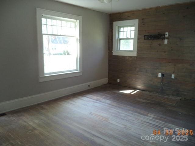 spare room featuring wooden walls, baseboards, and wood finished floors