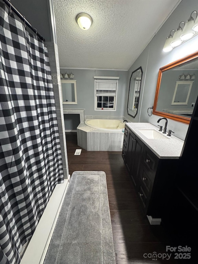 bathroom with a textured ceiling, wood finished floors, vanity, a bath, and a shower with curtain