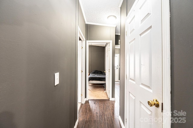 corridor with ornamental molding, dark wood-style flooring, and a textured ceiling