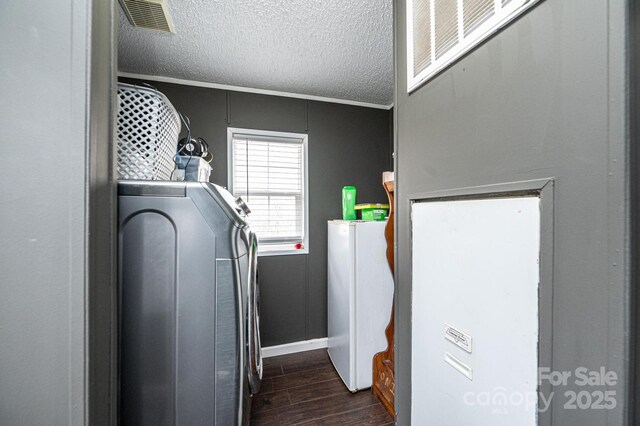 laundry area featuring dark wood-type flooring, a textured ceiling, ornamental molding, washer and dryer, and baseboards