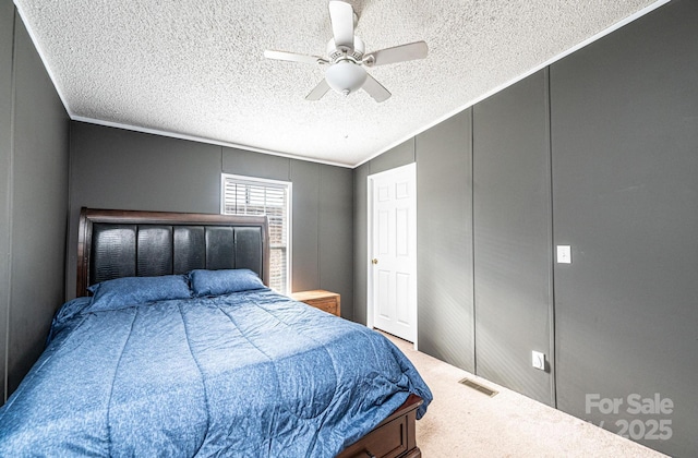 bedroom with a decorative wall, a textured ceiling, ornamental molding, carpet, and ceiling fan