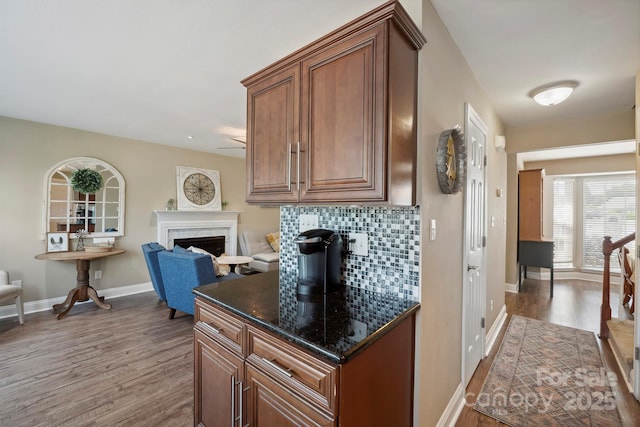kitchen featuring brown cabinetry, wood finished floors, a fireplace, baseboards, and backsplash