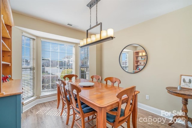 dining space with light wood-style floors, baseboards, a healthy amount of sunlight, and visible vents