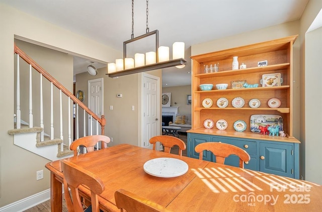 dining space with baseboards, a fireplace, wood finished floors, and stairway