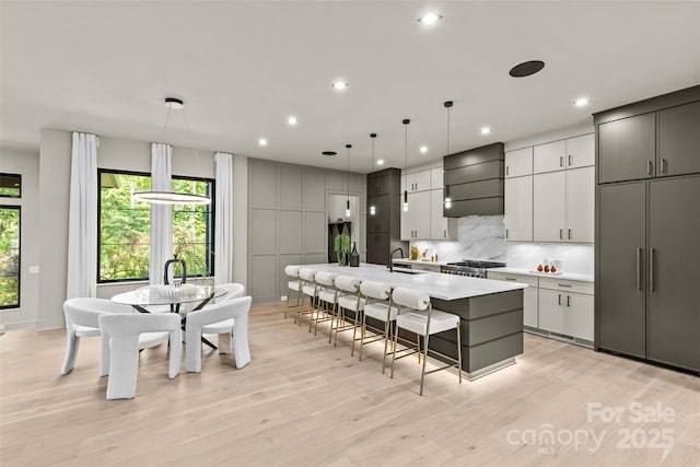 624 Heather Ln, Charlotte, NC 28209 - kitchen with custom exhaust hood, a center island with sink, light wood finished floors, backsplash, and recessed lighting