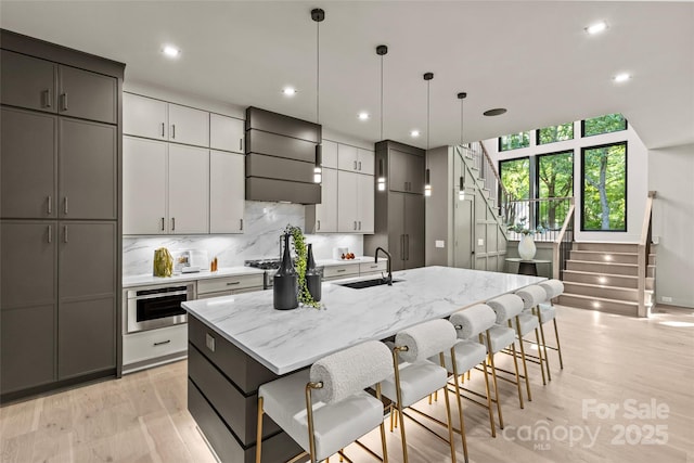 624 Heather Ln, Charlotte, NC 28209 - kitchen with premium range hood, a kitchen island with sink, stainless steel oven, a breakfast bar, and light wood-style flooring