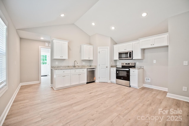 kitchen with appliances with stainless steel finishes, a sink, white cabinetry, baseboards, and lofted ceiling