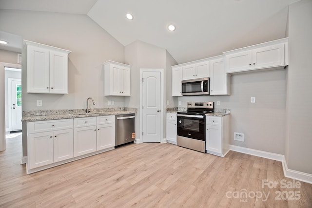 kitchen featuring appliances with stainless steel finishes, a sink, white cabinets, light wood finished floors, and lofted ceiling