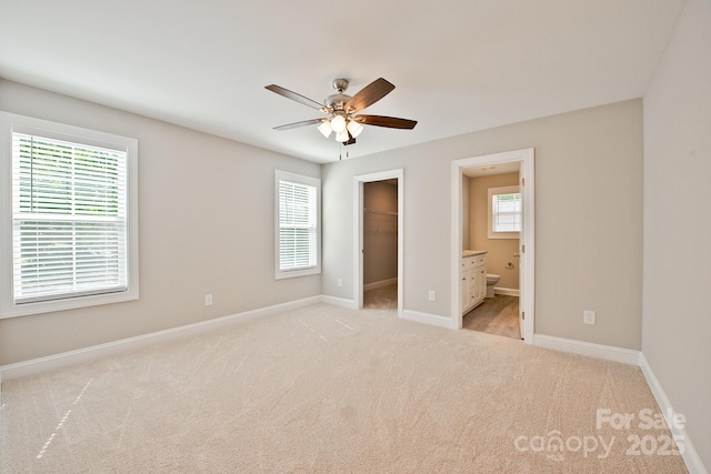 unfurnished bedroom with light carpet, baseboards, ensuite bathroom, a spacious closet, and a closet