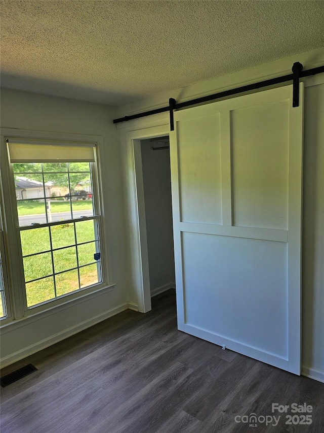 1109 Reid Harkey Rd, Matthews, NC 28105 - unfurnished bedroom featuring a barn door, dark wood-style flooring, a textured ceiling, and baseboards