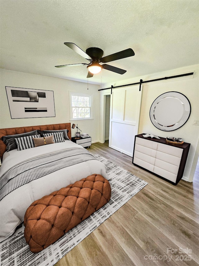1109 Reid Harkey Rd, Matthews, NC 28105 - bedroom with a barn door, wood finished floors, a textured ceiling, a ceiling fan, and baseboards