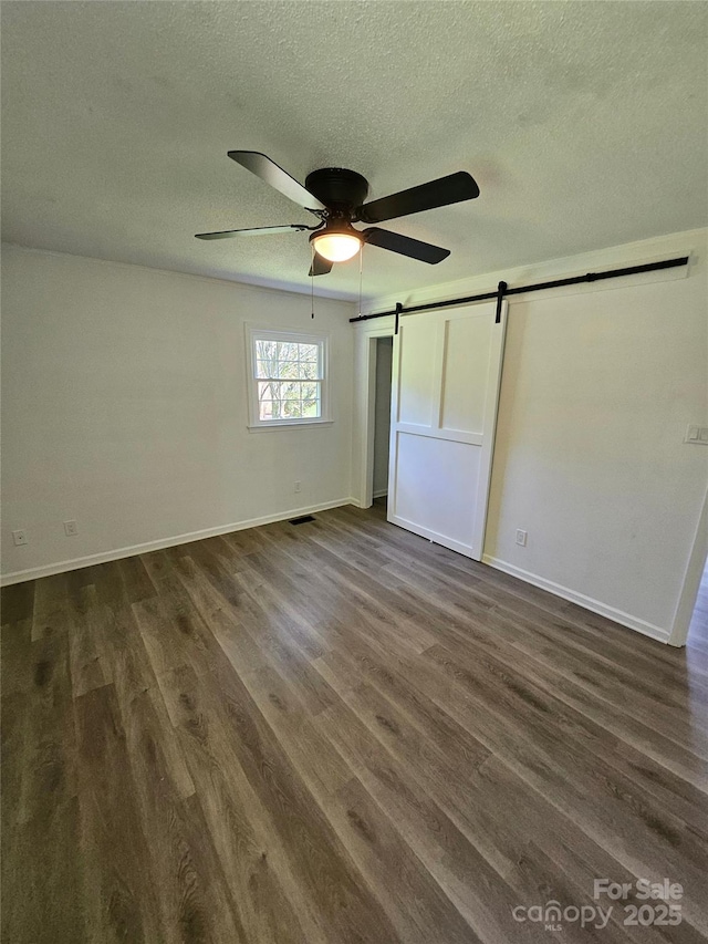 1109 Reid Harkey Rd, Matthews, NC 28105 - unfurnished bedroom with a barn door, a textured ceiling, dark wood finished floors, baseboards, and a ceiling fan